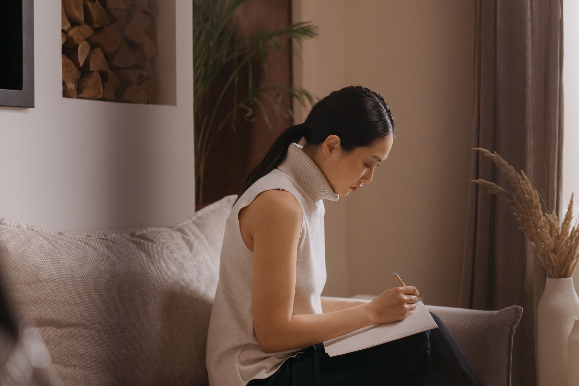 Naomi Ortega writing in her notebook on a couch in a quiet, warmly lit room